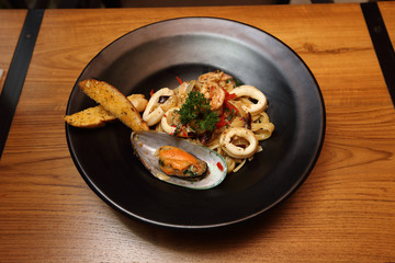 Seafood pasta, shell, shrimp, squid in black circle bowl on wooden table, top view