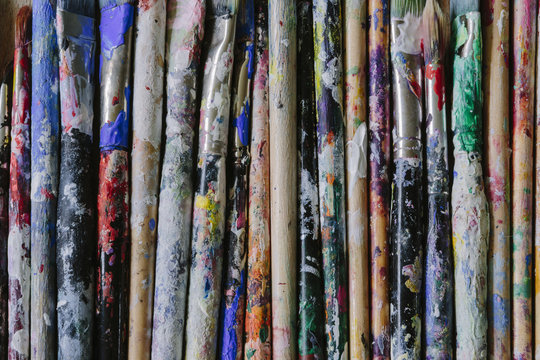Used paint brushes with multicoloured handles laying in a row