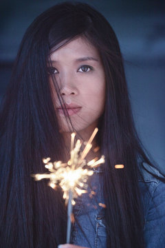 Asian woman with flying hair holding sparkler.