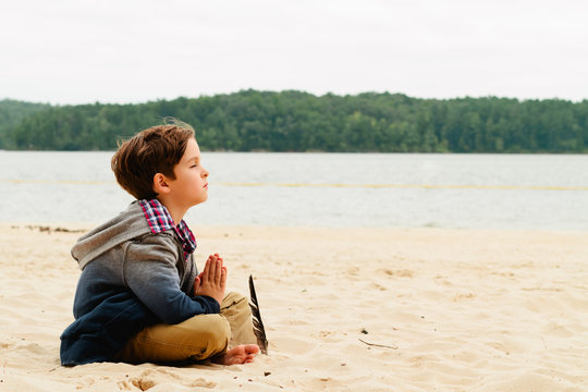 young boy meditating, praying on the beach
