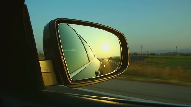 Highway road travel seen from side mirror with a sunrise sunset