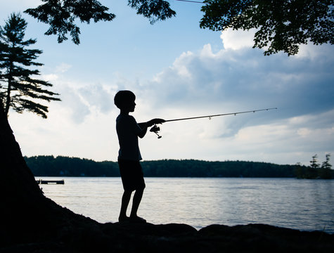 Silhouette of a boy fishing on a lake at sunset