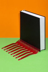 Still life with a black book and red forks on a colored background