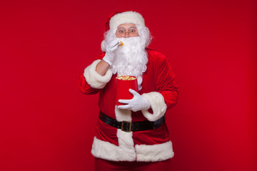 Traditional Santa Claus watching TV, eating popcorn. Christmas. Red background. emotions fear surprise