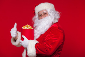 Traditional Santa Claus watching TV, eating popcorn. Christmas. Red background. emotions fear surprise
