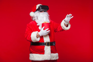 Santa Claus wearing virtual reality goggles and a red bucket with popcorn, on a red background. Christmas