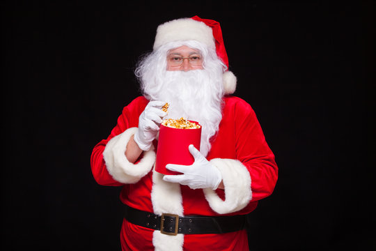 Christmas. Photo of Santa Claus gloved hand With a red bucket with popcorn, on a black background