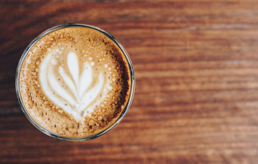 A cup of hot coffee with latte art on the wooden table.