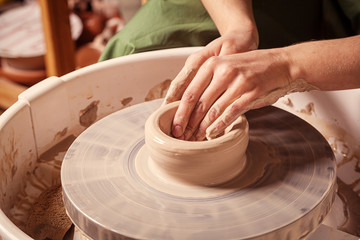 Close-up of a young woman potter beautifully sculpts a brown clay vase and makes for her neck on a potter's wheel, a top view
