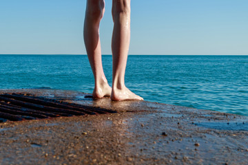 the legs of a man standing on an old stone pier before jumping into the sea