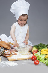 Caucasian Girl In Cook Uniform Working With Kitchen Glassware with Whisk In Studio Environment. With Vegetables and Fruits on Background.