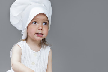 Portrait of Caucasian Little Girl in Cook Uniform Posing with Smudgy Face Against Gray Background