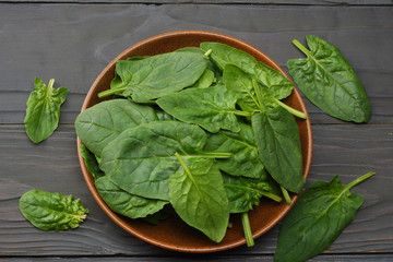 spinach leaves in bowl on dark wooden table top view