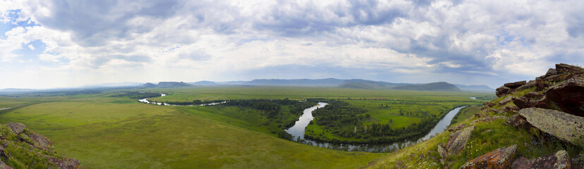 Obraz premium A large panorama of a beautiful green meadow with mountains in the background and a river along its entire length. The river valley with green beaches.