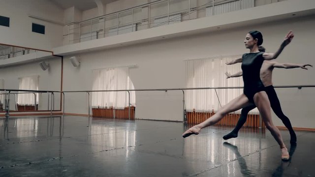 Young man practicing in classical ballet with young beautiful woman in black clothing in the gym. Minimalism interior, sensual dance. Slow motion. adagio