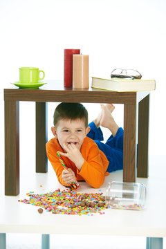 Happy kid eating sweets under table at home