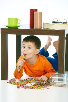 Happy kid eating lollipop under table sweets spilt