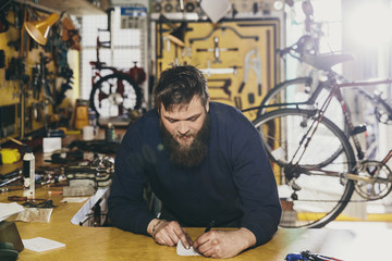 Young mechanic writing on a paper in a workshop