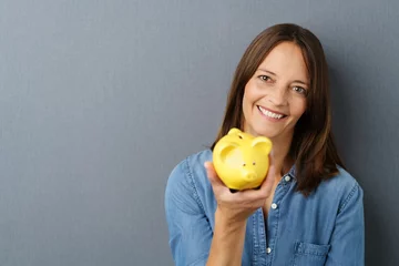Foto op Plexiglas lächelnde frau zeigt ein gelbes sparschwein © contrastwerkstatt