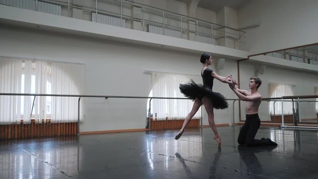 Young man practicing in classical ballet with young beautiful woman in black tutu clothing in the gym. Slow motion. A young couple performs a dance in a ballet school