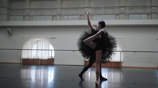 Young man practicing in classical ballet with young beautiful woman in black tutu clothing in the gym. Slow motion. A young couple performs a dance in a ballet school