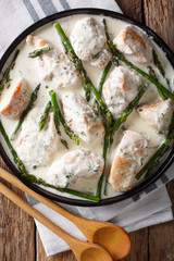 Chicken fillet with asparagus in a creamy sauce close-up on a plate. Vertical top view
