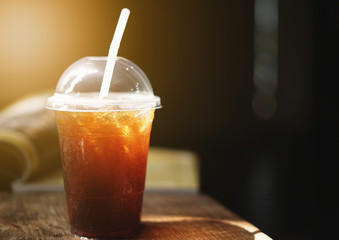 Cold iced black coffee with book on wooden table background.