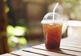 Cold iced black coffee on wooden table in the garden background.