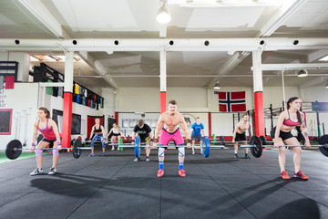 Determined Trainer With Athletes Lifting Barbells In Gym