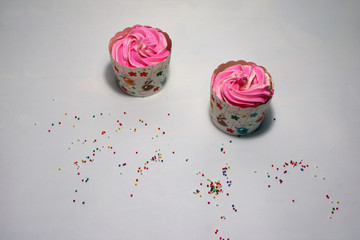 Two birthday cup cake on the white background with colorful rounded sugar beads. cupcake is a small cake baked in a cup-shaped container.