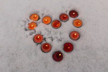 bright multicolored burning candles lined in the shape of a heart in the snow