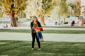 Happy young mother playing with toddler boy in a nice sunny park on fall warm day. Woman having good time with a son