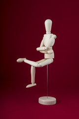 a wooden mannequin in sitting position with a red  background	