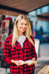 Happy young blond reading woman in a book store, wearing red plaid shirt
