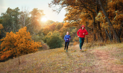 Fototapeta premium coupe of athletes in black leggins and color jacket run on a jogging on the colorful autumnal forest