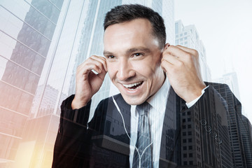 Cheerful happy businessman putting headphones into his ears