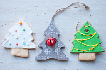Three Christmas toys in the shape of Christmas tree. The green and white trees are gingerbread cookies, the gray tree is a wooden christmas toy.