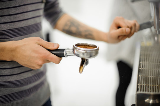 Barista with tattoo holding a temper with coffee