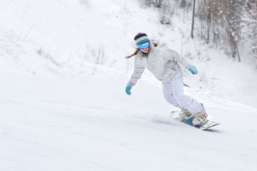 Young woman snowboarder in motion on snowboard in mountains