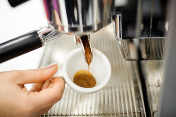 Pouring fresh coffee into a small white coffee cup