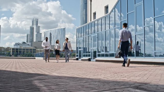 Multi-ethnic business team walking together in downtown at sunny day and discussing something