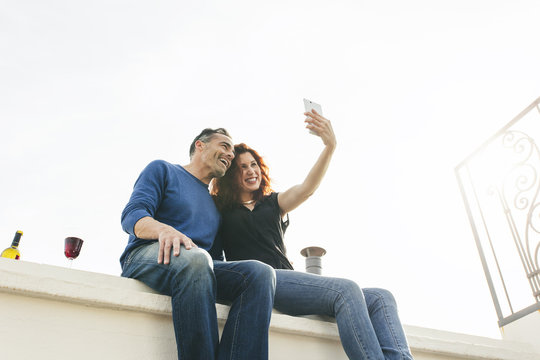 Beautiful couple taking a picture of themselves with smart phone on the rooftop.