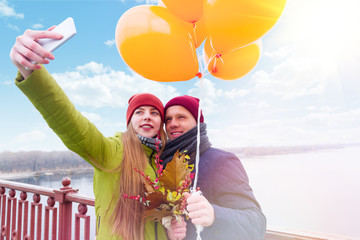 Obraz premium Couple with yellow balloons doing selfie by smartphone in dating in autumn