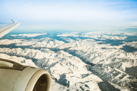 Fototapeta Aerial view of European Alps with misty horizon and part of airplane wing engine - Travel concept and winter vacation on white snow mountains - Trip wander to exclusive luxury destinations worldwide