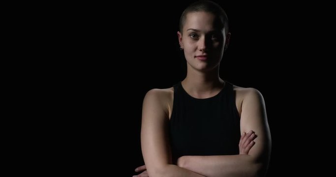 Young short haired woman steps out of the dark and crosses arms