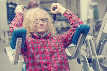Skinny guy with glasses and with curly blond hair exercising in the gym