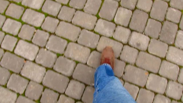 Men's legs shod in sneakers walking along pavement with sidewalk tiles in city. Top view.