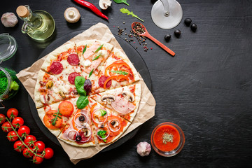Pizza with ingredients, spices, oil and vegetables on dark table. Flat lay, top view.