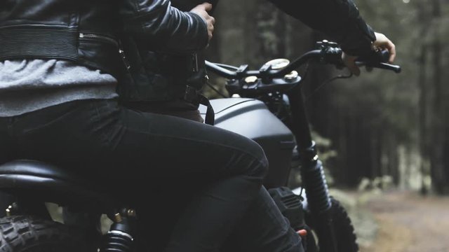 Man and woman couple riding custom built cafe racer motorcycle on a forest road.