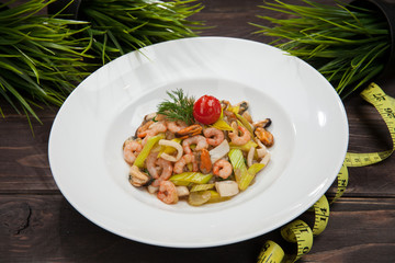 salad from greens and shrimps on a wooden black table, and a centimeter ribbon, healthy food, fitness menu